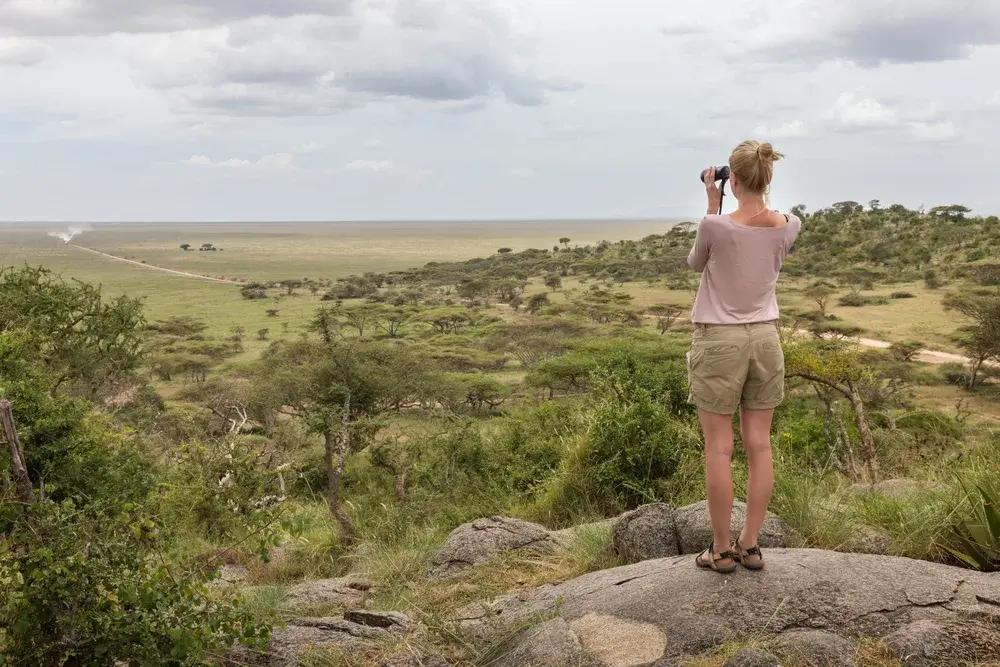 Woman looking through a pair of binoculars over an expansive forest during the best time to visit Tanzania