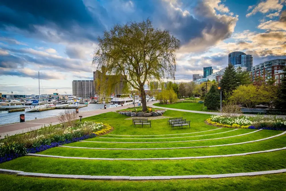 Toronto music garden pictured during the best time to visit, the spring, with gorgeous clouds on the horizon and boats in the harbor