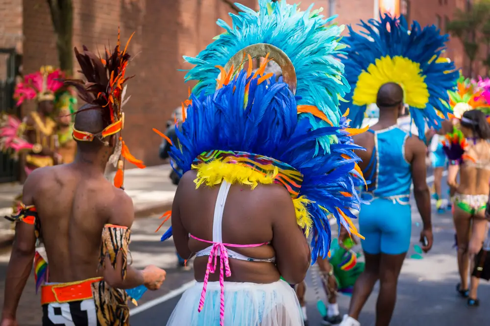 Carnival parade participants wearing colorful feathers walk in the parade during February, one of the worst times to visit Trinidad if you want to avoid crowds