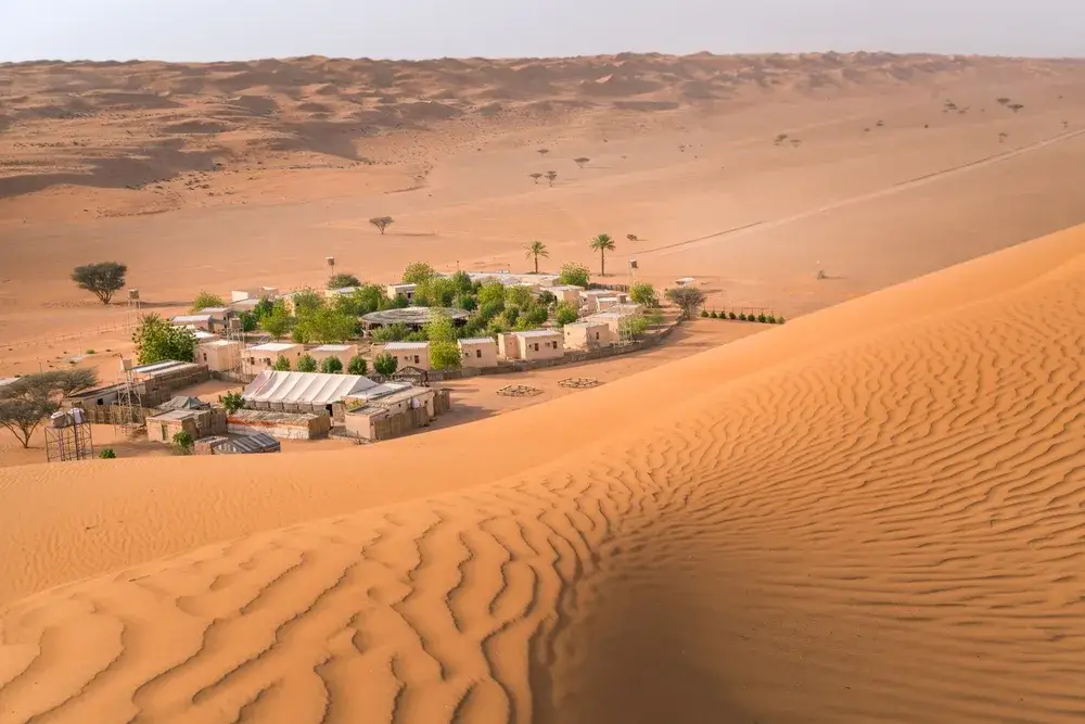 Small Bedouin camp with trees in the middle and desert sand and dunes all around pictured during the summer, the overall worst time to visit Oman