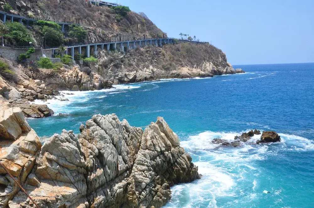 For a piece titled Is Acapulco Safe to Visit, a beach shot of a bridge and road overlooking the ocean