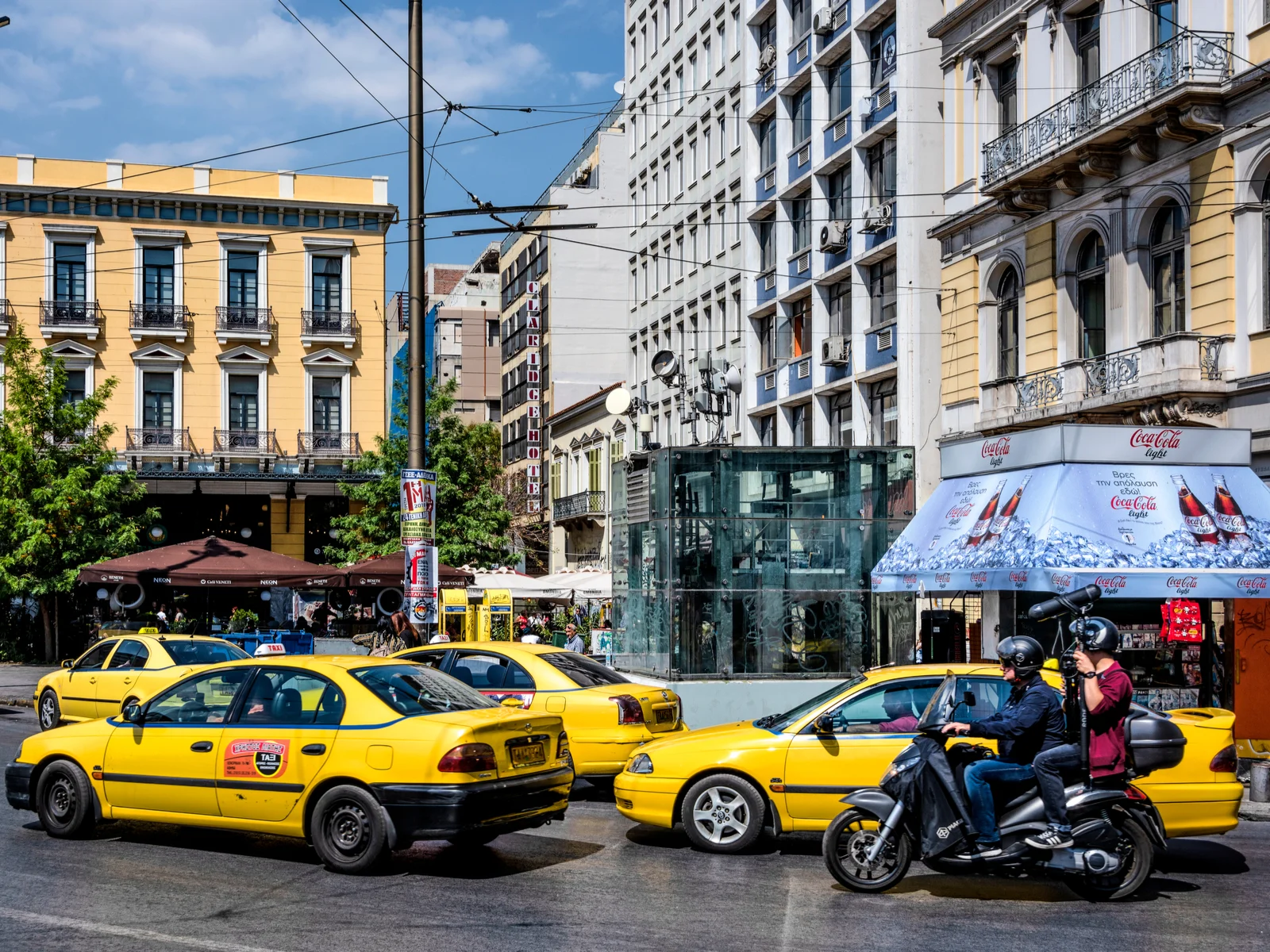 Omonia town square with taxis in the middle of buildings on a clear day for a piece titled Is Greece Safe