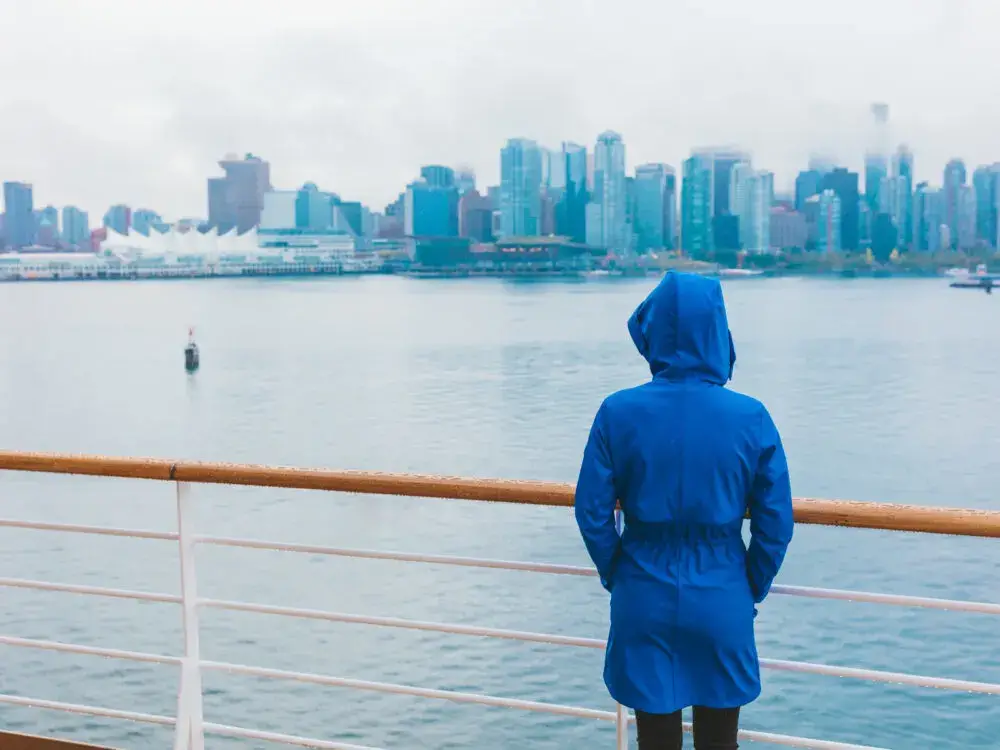 Woman standing on the edge of the ferry on a foggy day during the worst time to visit Seattle with the buildings in the back obscured by fog