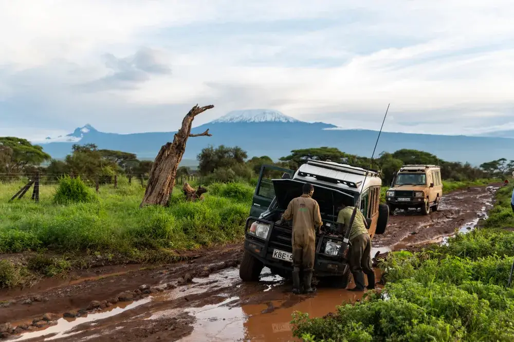 Two guys in Africa pushing a car out of a muddy dirt path during the rainy season, the worst time to visit Kenya