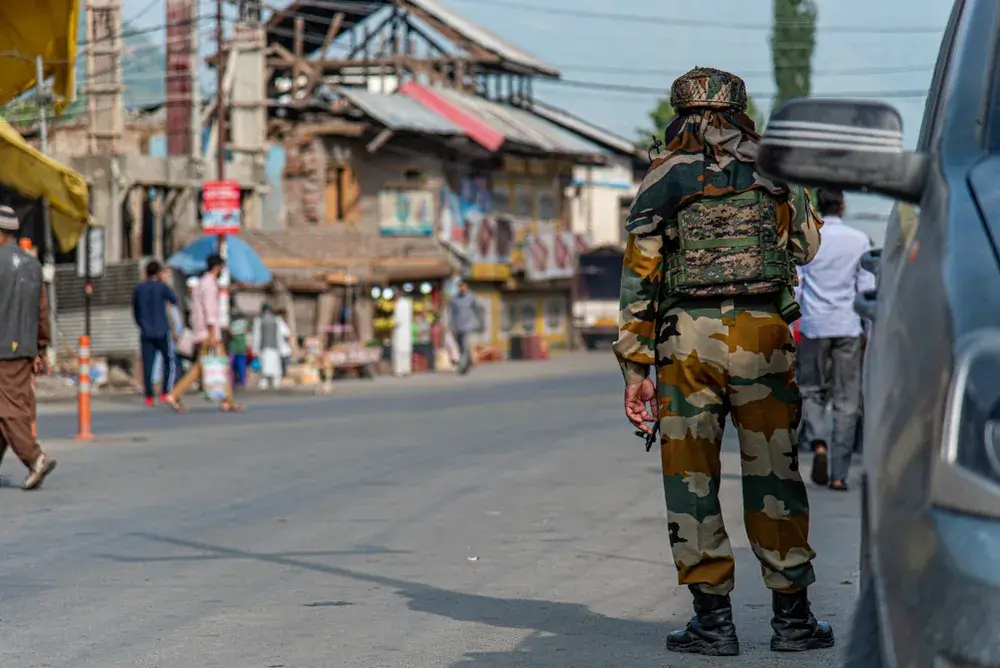 Man in fatigues pictured standing next to a military vehicle for a piece titled Is India Safe to Travel to