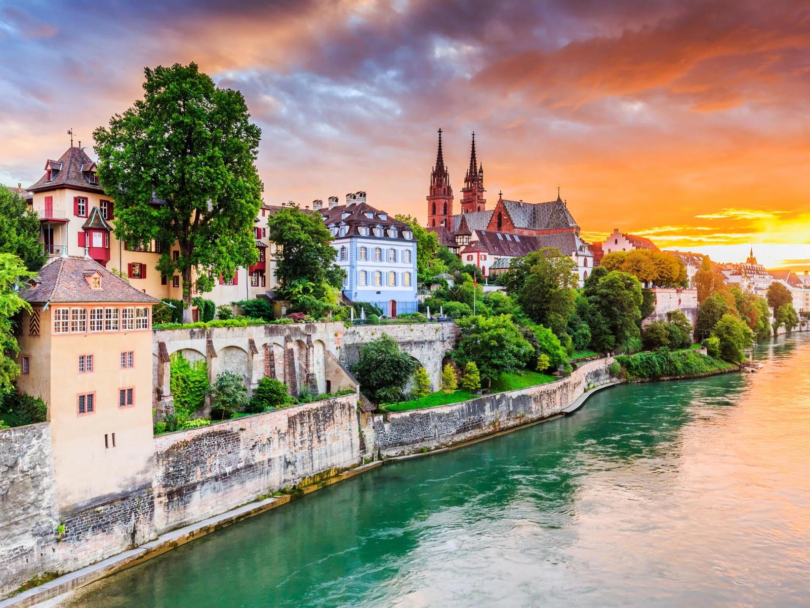 Oceanfront photo of Basel with red stone and the Munster cathedral on the Rhine River pictured during the least busy time to visit Switzerland