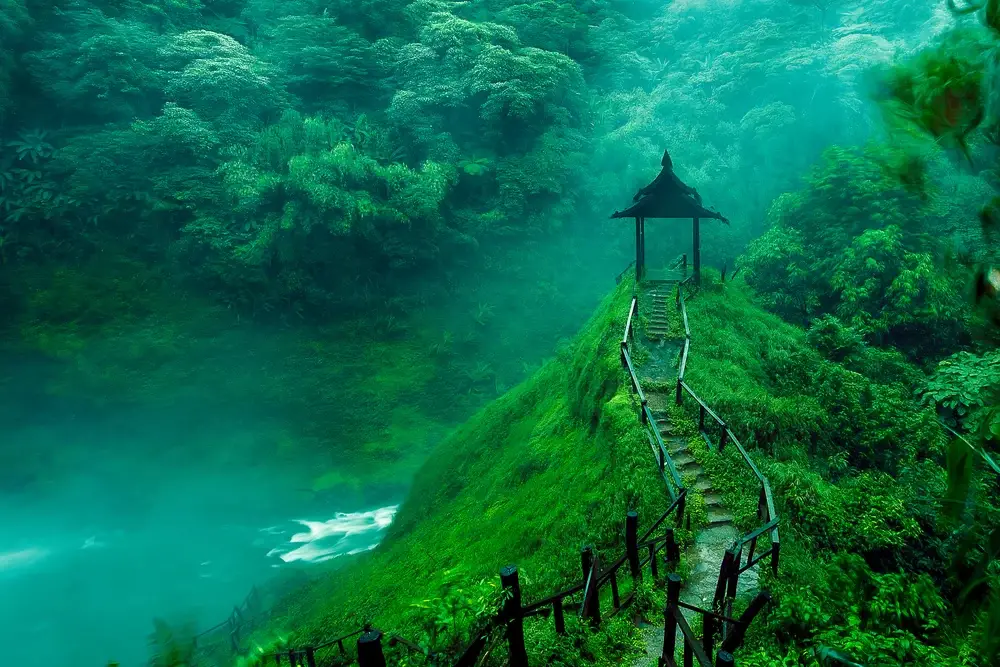 Gorgeous waterfalls in Laos pictured during the cheapest time to visit, with fog and mist above a viewing platform made of wood