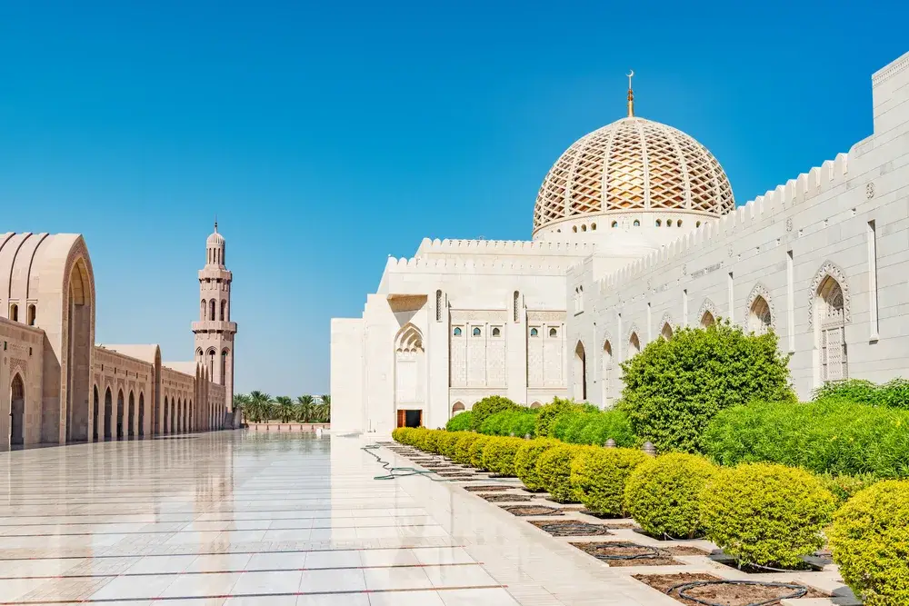 Gorgeous white marble mosque in Muscat for a piece on if Oman is safe to visit, with green shrubs alongside the detailed wall