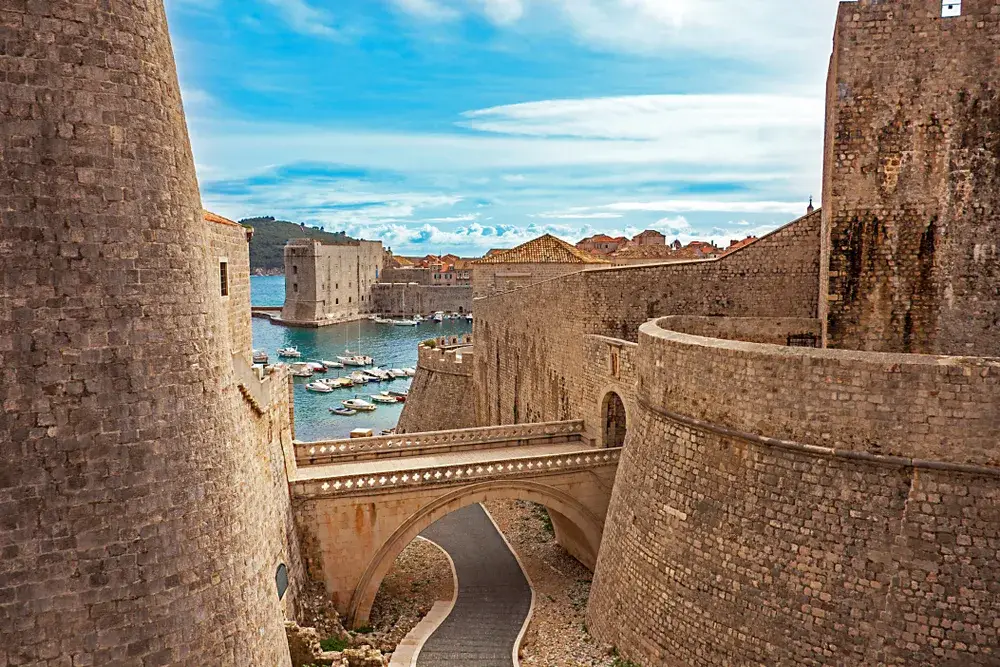 Photo of the old town harbor in Dubrovnik pictured with a stone bridge going over the walkway leading to the water