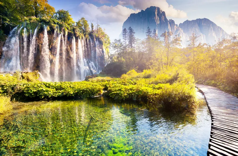 Awe-inspiring view of the waterfalls at Plitvice Lakes National Park with a wooden walkway leading over still water for a piece on the best places to visit Croatia