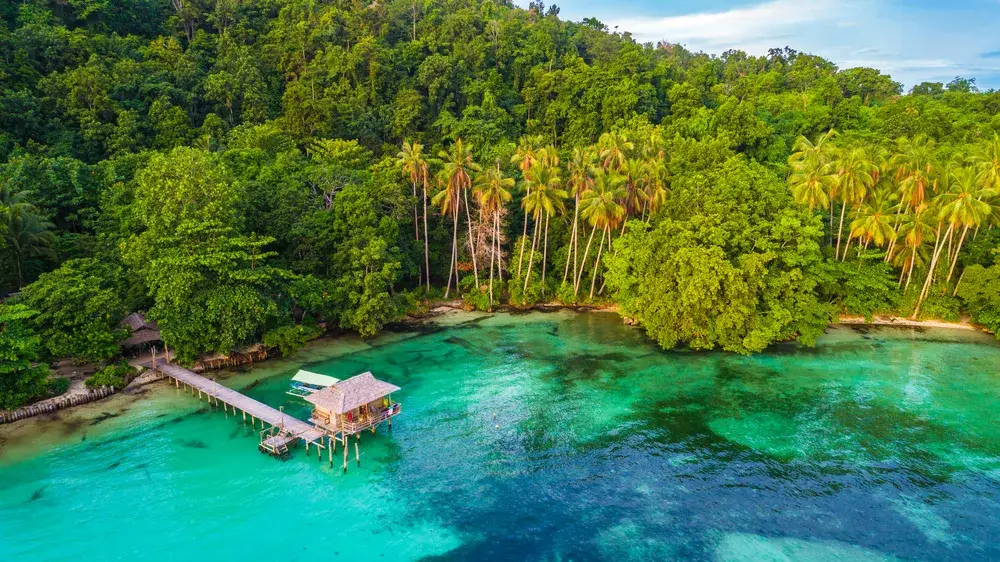 Hut just off the beach on stilts overlooking crystal-clear water in West Papau during the cheapest time to visit Indonesia