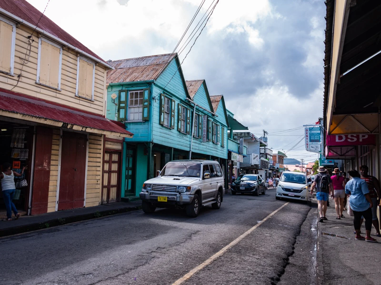 Cars driving down the street for a piece titled Is Antigua Safe featuring buildings on either side of the road