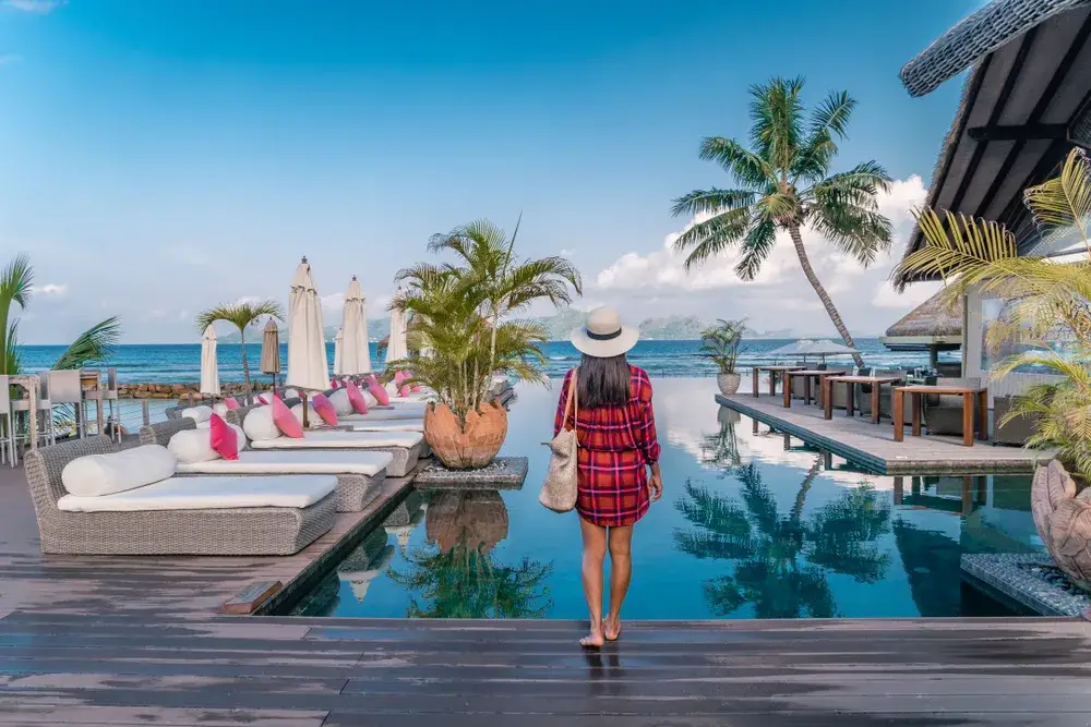 Young model in a black and red striped shirt pictured standing by a pool at a resort in the Seychelles