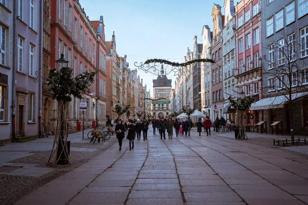 People walking along the street during the winter during the worst time to visit Poland in Gdansk with bricks on the ground and gloomy skies with Christmas decorations all around