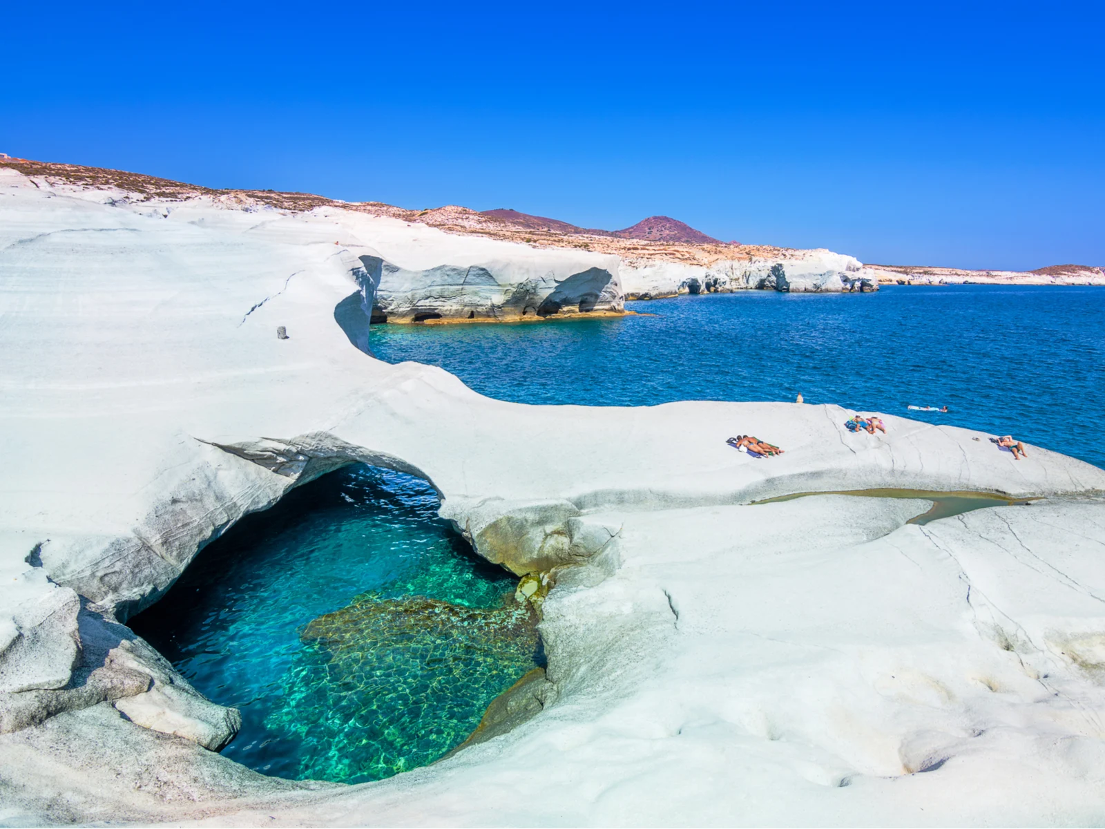 Sarakiniko, Milos, one of the best beaches in Greece, as seen from the top of the rocks with sunbathers next to the blue water