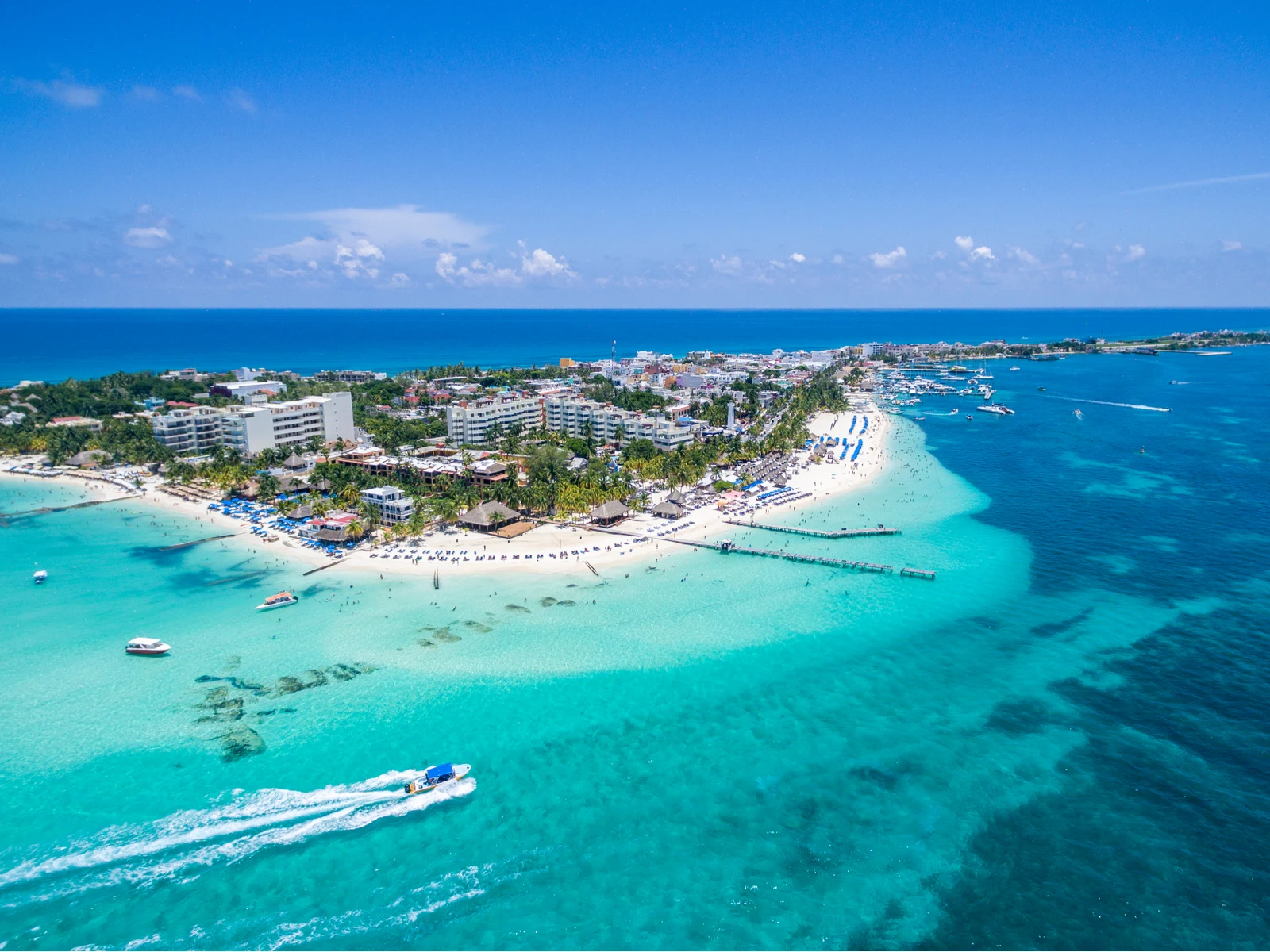 Aerial view of Isla Mujeres' white sand Playa Norte, one of the best beaches in Cancun, with its tall hotel buildings and residential area, and a speed boat passing by its vicinity