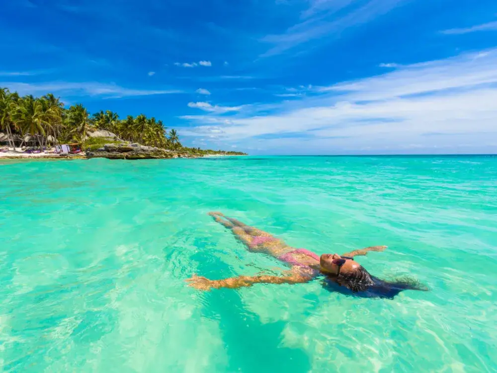 Thin woman in a bikini floating in green water during the best time to visit the Caribbean