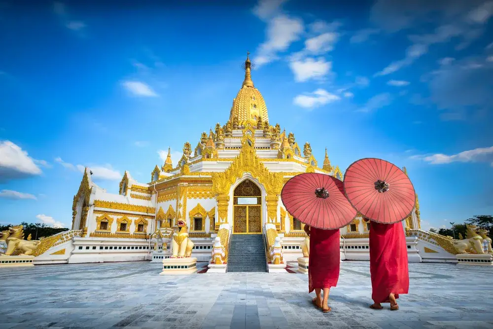 Swe taw myat pagoda pictured on a sunny day in back of people in red robes holding paper umbrellas for a piece on is Myanmar safe to visit