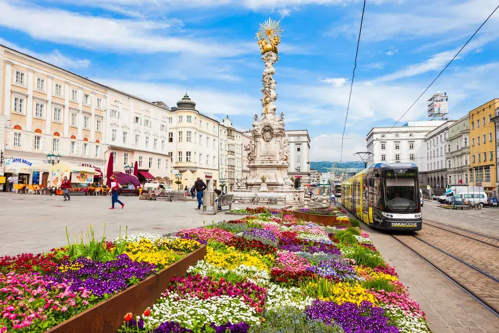 Electric tram at a station surrounded by statues and gorgeous historic buildings in Linz, one of the best places to visit in Austria