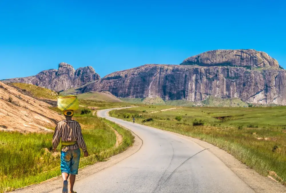 Betsileo person walking on a road with a basket on her head pictured during the cheapest time to visit Madagascar