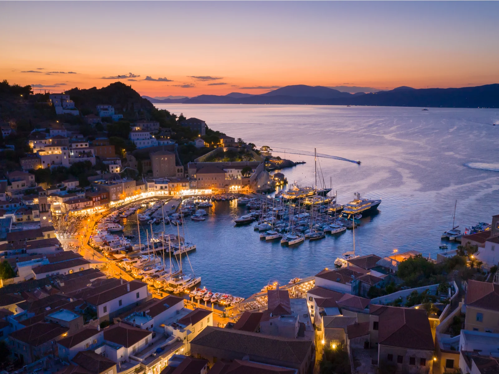 Several boats docked at a gulf-like pier at Hydra island, one of the best islands in Greece to visit, on a beautiful and calm dusk