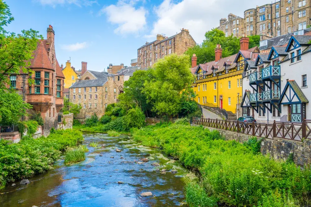 Gorgeous sunny day in Edinburgh as seen from the banks of the river in Dean Village with the river running down the middle of a canal with historic homes on either side