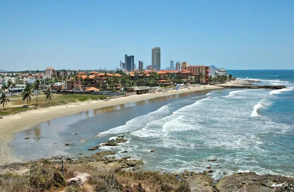 Picturesque aerial view of Mazatlan, taken during the best time to visit, with few tourists on the beach and waves lightly lapping the shoreline with blue skies above