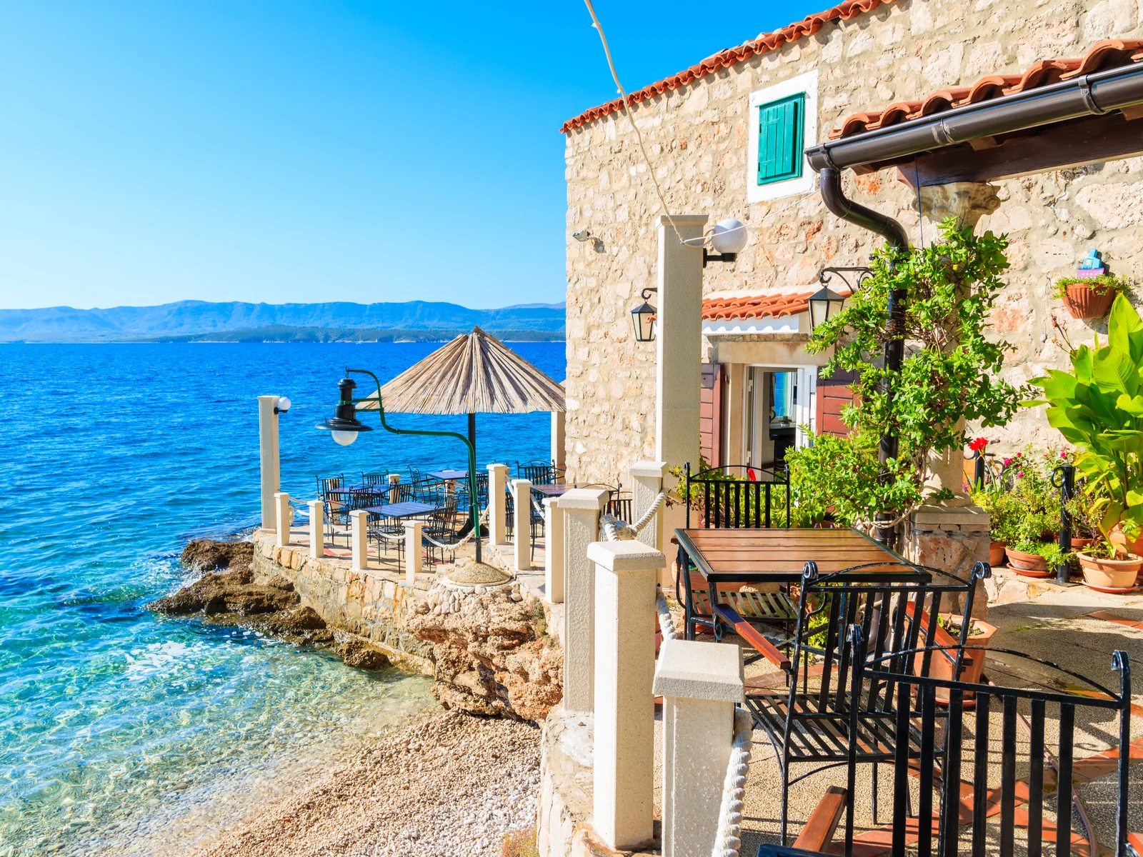 Small restaurant in Bol during the best time to visit Croatia, the summer, with blue skies and crystal clear teal water